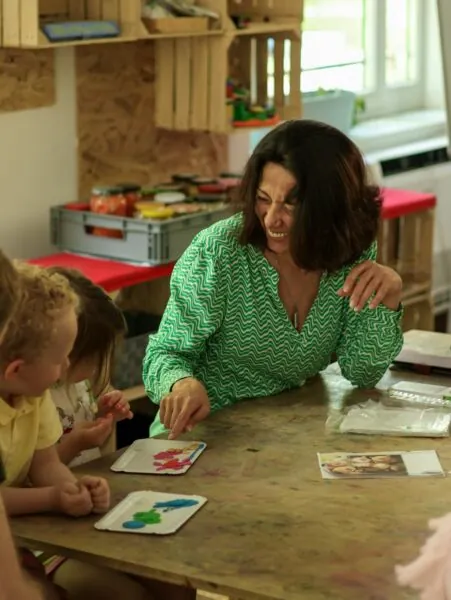 A woman in a green patterned shirt pointing at clay shapes with two children