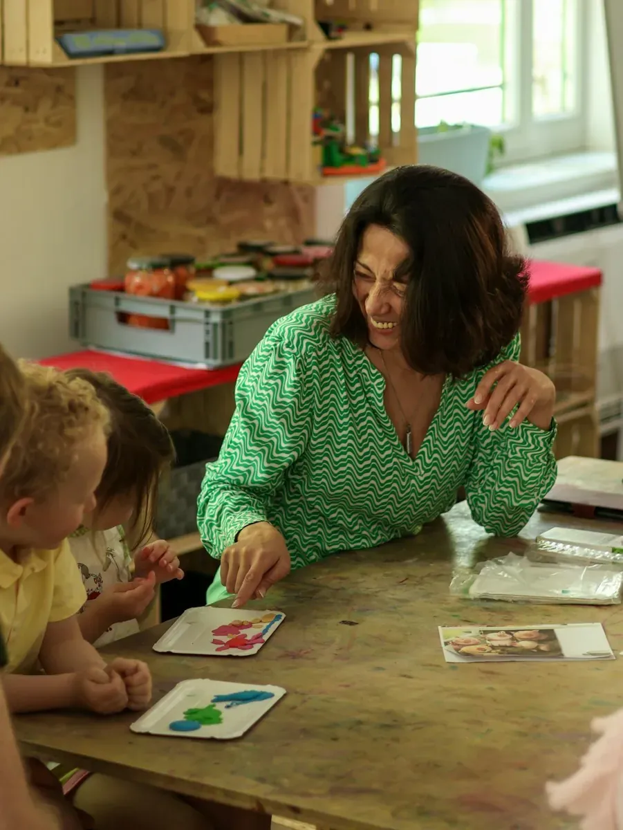 A woman in a green patterned shirt pointing at clay shapes with two children